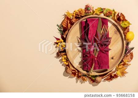 Autumn thanksgiving table place setting with cutlery, wooden plate and arrangement of fall leaves Autumn thanksgiving table place setting with cutlery, wooden plate and arrangement of fall leaves 93668158