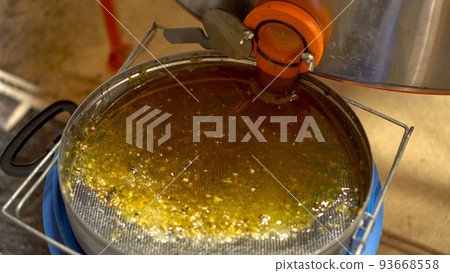 Honey in a metal tank flows through a pipe. Honey is filtered through a sieve after extraction. 93668558