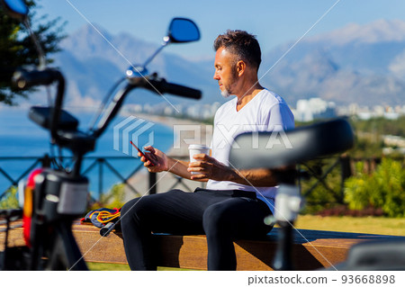 old-aged man good loking outdoors with eco scooter using the application on smartphone old-aged man good loking outdoors with eco scooter using the application on smartphone 93668898