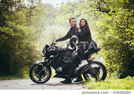 Handsome young man and beautiful young girl, couple sitting on a motorcycle, standing near a motorcycle in black leather clothes, hugging, in nature, on the street Handsome young man and beautiful young girl, couple sitting on a motorcycle, standing near a motorcycle in black leather clothes, hugging, in nature, on the street 93668899