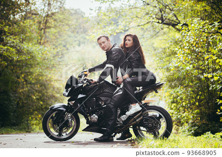 Handsome young man and beautiful young girl, couple sitting on a motorcycle, standing near a motorcycle in black leather clothes, hugging, in nature, on the street Handsome young man and beautiful young girl, couple sitting on a motorcycle, standing near a motorcycle in black leather clothes, hugging, in nature, on the street 93668905