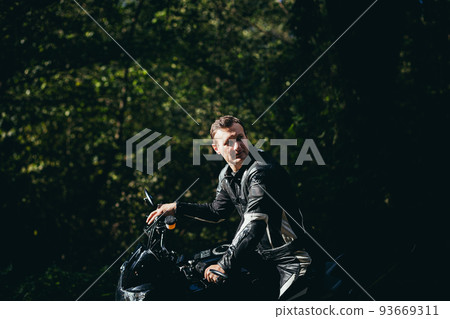 Handsome young man sitting rides a motorcycle in black leather clothes, looks at the camera, in full growth, on the run, on the road Handsome young man sitting rides a motorcycle in black leather clothes, looks at the camera, in full growth, on the run, on the road 93669311