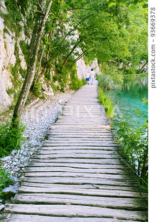 Summer landscapes along green lake in traveling journey. Wooden bridge walkway. Tourist walk. 93669378