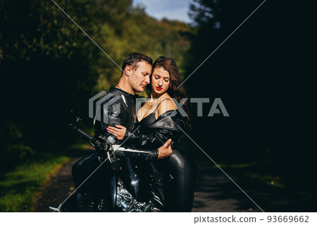 Handsome young man and beautiful young girl, couple sitting on a motorcycle, standing near a motorcycle in black leather clothes, hugging, in nature, on the street Handsome young man and beautiful young girl, couple sitting on a motorcycle, standing near a motorcycle in black leather clothes, hugging, in nature, on the street 93669662
