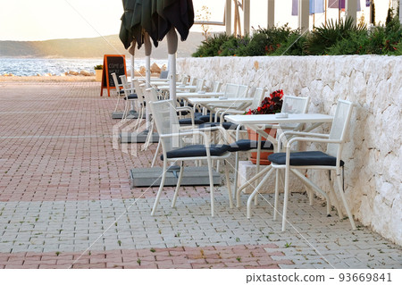 Seating area in summer in recreation by the sea. White table and armchairs on outdoor terrace of summer cafe. Restaurant business awaits visitors. 93669841