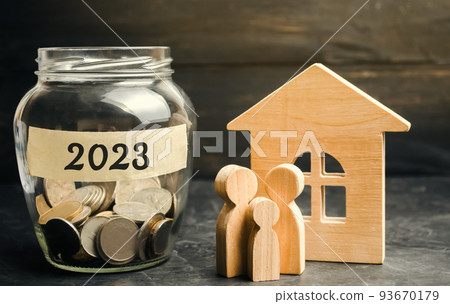 Family budget planning concept. Investments, plans, savings. Mortgage rates. Real estate. Glass jar with coins 2023 and family near the wooden house Family budget planning concept. Investments, plans, savings. Mortgage rates. Real estate. Glass jar with coins 2023 and family near the wooden house 93670179