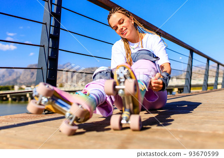 Photo of cheerful young happy woman wear white t-shirt and bell-bottomed trousers with pink pastel color roller skates outdoors in sunny day 93670599