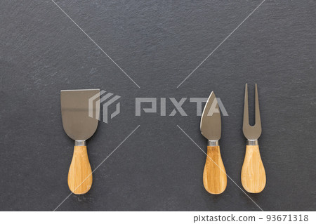 Set of cheese knives with wooden handles. Fork and spatula on black background. Shabby appearance. Top view, copy space 93671318