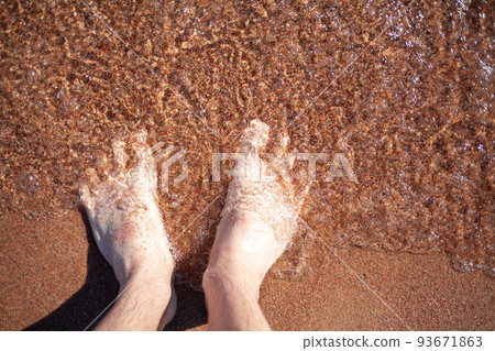 Top view of men's legs in the sea. A man is standing on the sand. 93671863