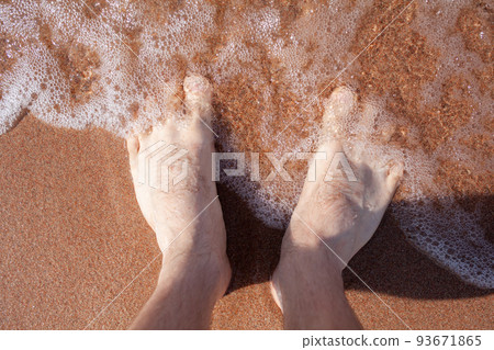 Top view of men's legs in the sea. A man is standing on the sand. Top view of men's legs in the sea. A man is standing on the sand. 93671865