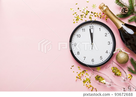 New year celebration concept with a bottle of champagne and two glasses toasting. Christmas gift box, alarm clock and fir tree branch on colored table. Top view Copy space New year celebration concept with a bottle of champagne and two glasses toasting. Christmas gift box, alarm clock and fir tree branch on colored table. Top view Copy space 93672688
