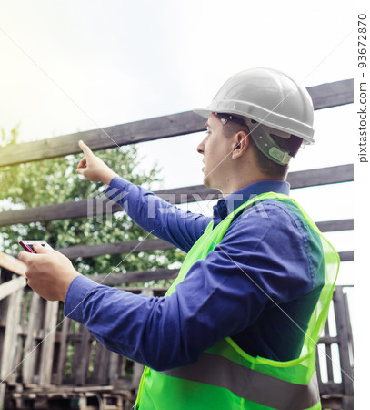 Building inspector. Man in a hard hat and a yellow reflective vest examines damaged structures and inspects the building. Damage assessment. Preparing for the repair or construction of a building 93672870