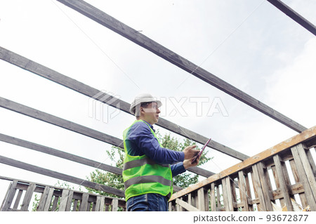 Building inspector. Man in a hard hat and a yellow reflective vest examines damaged structures and inspects the building. Damage assessment. Preparing for the repair or construction of a building Building inspector. Man in a hard hat and a yellow reflective vest examines damaged structures and inspects the building. Damage assessment. Preparing for the repair or construction of a building 93672877