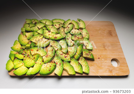 Avocado slices on a wooden textured background sprinkled with spices, bright accent. View from above Avocado slices on a wooden textured background sprinkled with spices, bright accent. View from above 93673203