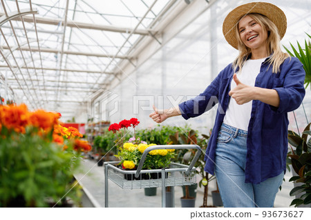 Woman with a basket of flowers showing thumbs up rejoicing in shopping in a greenhouse Woman with a basket of flowers showing thumbs up rejoicing in shopping in a greenhouse 93673627