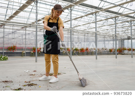 Woman sweeping the floor in a greenhouse with flowers 93673820