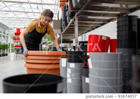 Pretty woman in uniform working in a shop with flower pots 93674057