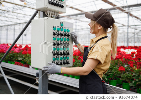 Female flowers greenhouse worker presses a button on a control panel to start the process of watering plants using an intelligent irrigation machine 93674074