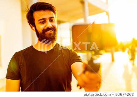 bearded man in black cotton t-shirt recording video for vegan blog outdoor in summer park at sunset gold light 93674268