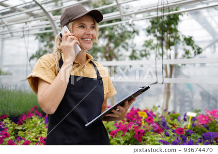 Pretty female florist with clipboard talking on the phone in a flower greenhouse 93674470