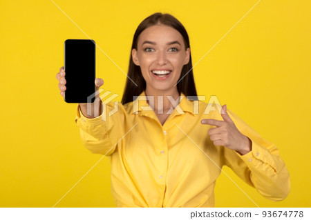 Happy Woman Showing Smartphone Empty Screen Over Yellow Background 93674778