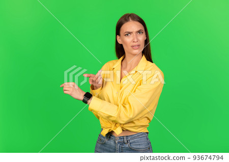 Displeased Female Pointing Finger At Smartwatch Over Green Studio Background 93674794