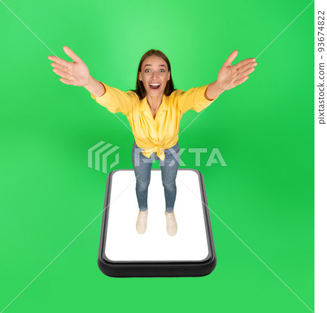 Excited Woman Standing On Huge Smartphone Screen Over Green Background 93674822