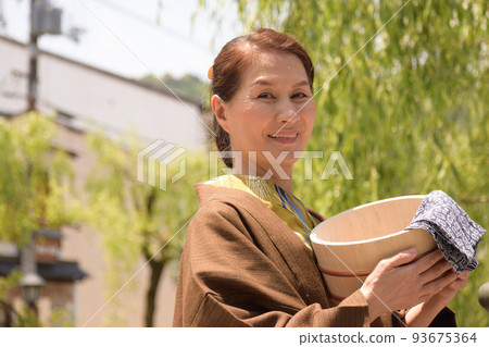 A smiling senior woman wearing a yukata, holding a hot tub, and visiting the hot springs of Kinosaki Onsen A smiling senior woman wearing a yukata, holding a hot tub, and visiting the hot springs of Kinosaki Onsen 93675364