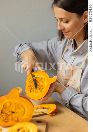 woman cuts orange pumpkins with a knife on a cutting board in the kitchen. cooking pumpkin is an eco-friendly food for the whole family woman cuts orange pumpkins with a knife on a cutting board in the kitchen. cooking pumpkin is an eco-friendly food for the whole family 93675486