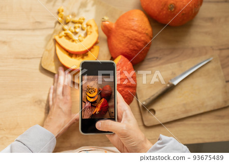 woman takes pictures of orange pumpkins on a cutting board in the kitchen. cooking pumpkin is an eco-friendly food for the whole family. 93675489