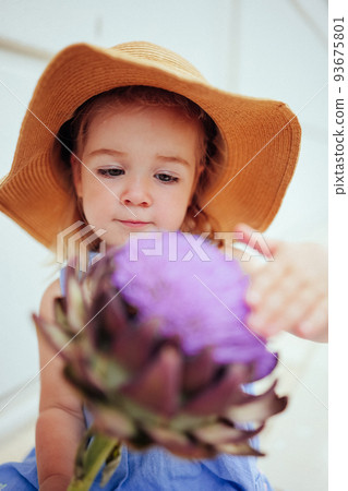 Cute little girl in straw hat touching big artichoke flower Cute little girl in straw hat touching big artichoke flower 93675801