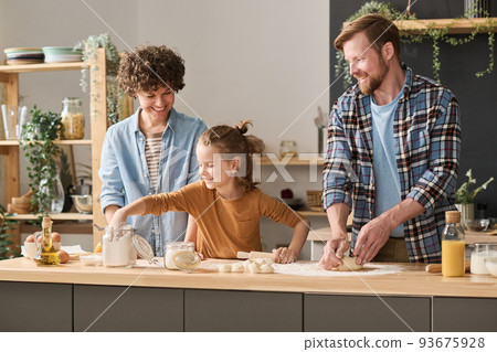 Little boy adding flour in dough and helping his parents to bake at table in kitchen 93675928