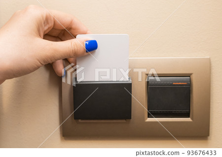 Woman hand puts key card to panel to switch on electricity in hotel room 93676433