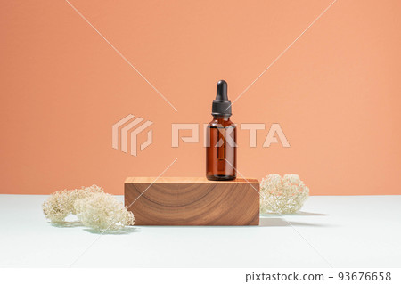 Bottle with pipette made of dark glass, cosmetic product woodenpedestal. Pastel coral background 93676658