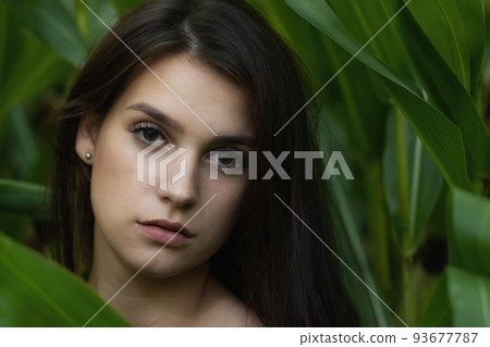 Long haired brunette young woman poses among the green plants Long haired brunette young woman poses among the green plants 93677787