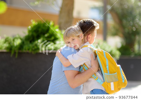 Little boy says goodbye and hugging to his father before going to school. Dad brought his son by car. Quality education for children. Child is a first day of school. Kids fear. Little boy says goodbye and hugging to his father before going to school. Dad brought his son by car. Quality education for children. Child is a first day of school. Kids fear. 93677844