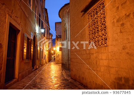 Empty illuminated street of Kotor old town at night off season. Historical buildings, cobblestone pavement, ancient churches are attraction for tourists in Montenegro on any season. 93677845