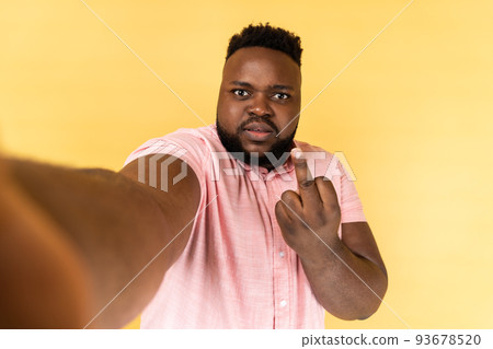 Portrait of serious aggressive man wearing pink shirt taking selfie, showing rude gesture with middle finger, point of view photo, POV. Indoor studio shot isolated on yellow background. Portrait of serious aggressive man wearing pink shirt taking selfie, showing rude gesture with middle finger, point of view photo, POV. Indoor studio shot isolated on yellow background. 93678520