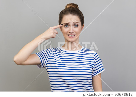 Crazy idea. Portrait of woman wearing striped T-shirt showing stupid gesture, looking with condemnation and blaming for insane plan, dumb suggestion. Indoor studio shot isolated on gray background. Crazy idea. Portrait of woman wearing striped T-shirt showing stupid gesture, looking with condemnation and blaming for insane plan, dumb suggestion. Indoor studio shot isolated on gray background. 93678612