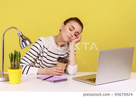 Sleepy woman office worker napping sitting at workplace with laptop on desk leaning head on hand, feeling boredom, lazy to work, overworking. Indoor studio studio shot isolated on yellow background. 93678924