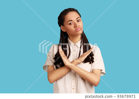 No way, never again. Portrait of determined serious woman with black dreadlocks crossing hands on chest, gesturing x sign, stop this is finish. Indoor studio shot isolated on blue background. 93678971