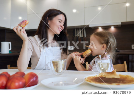 Crop shot of mother in red and her daughter having colorful donuts sitting at kitchen. Dieting concept and junk food. Crop shot of mother in red and her daughter having colorful donuts sitting at kitchen. Dieting concept and junk food. 93678979