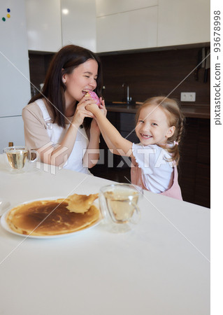 Crop shot of mother in red and her daughter having colorful donuts sitting at kitchen. Dieting concept and junk food. Crop shot of mother in red and her daughter having colorful donuts sitting at kitchen. Dieting concept and junk food. 93678998