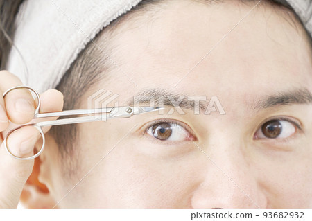 Close-up of a man cutting eyebrows with eyebrow scissors 93682932