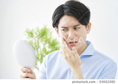 一個男人在家裡拿著一面手鏡，看著他的臉 93682980