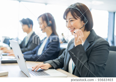 Woman doing customer support while wearing a headset at a call center Woman doing customer support while wearing a headset at a call center 93683403