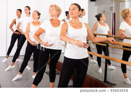 Group of women perform the battement tendu movement, standing in a ballet stance near the barre Group of women perform the battement tendu movement, standing in a ballet stance near the barre 93683859
