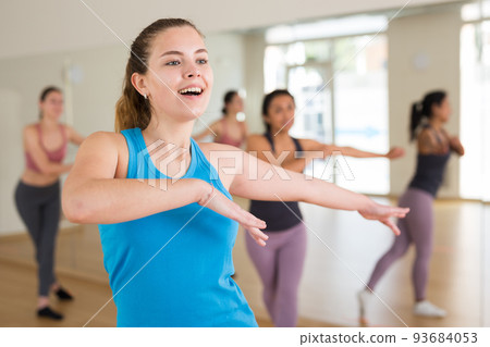 Smiling girl practicing vigorous swing during group training Smiling girl practicing vigorous swing during group training 93684053