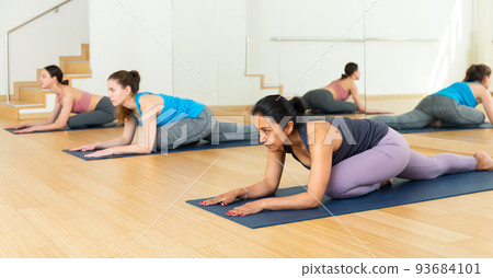 Group of women doing relaxing stretching workout in yoga studio Group of women doing relaxing stretching workout in yoga studio 93684101