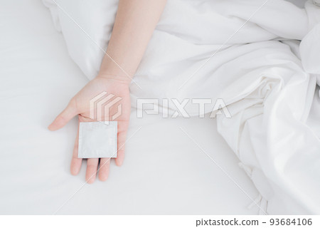 Cropped shot view of woman hand with condom on the bed. 93684106